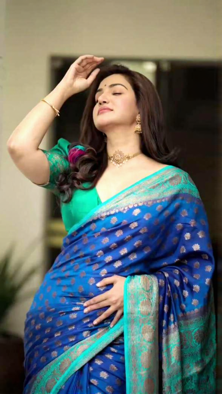 Royal blue Banarasi Silk saree with gold zari buttis and a teal contrast border, worn by a model in a natural light setting.