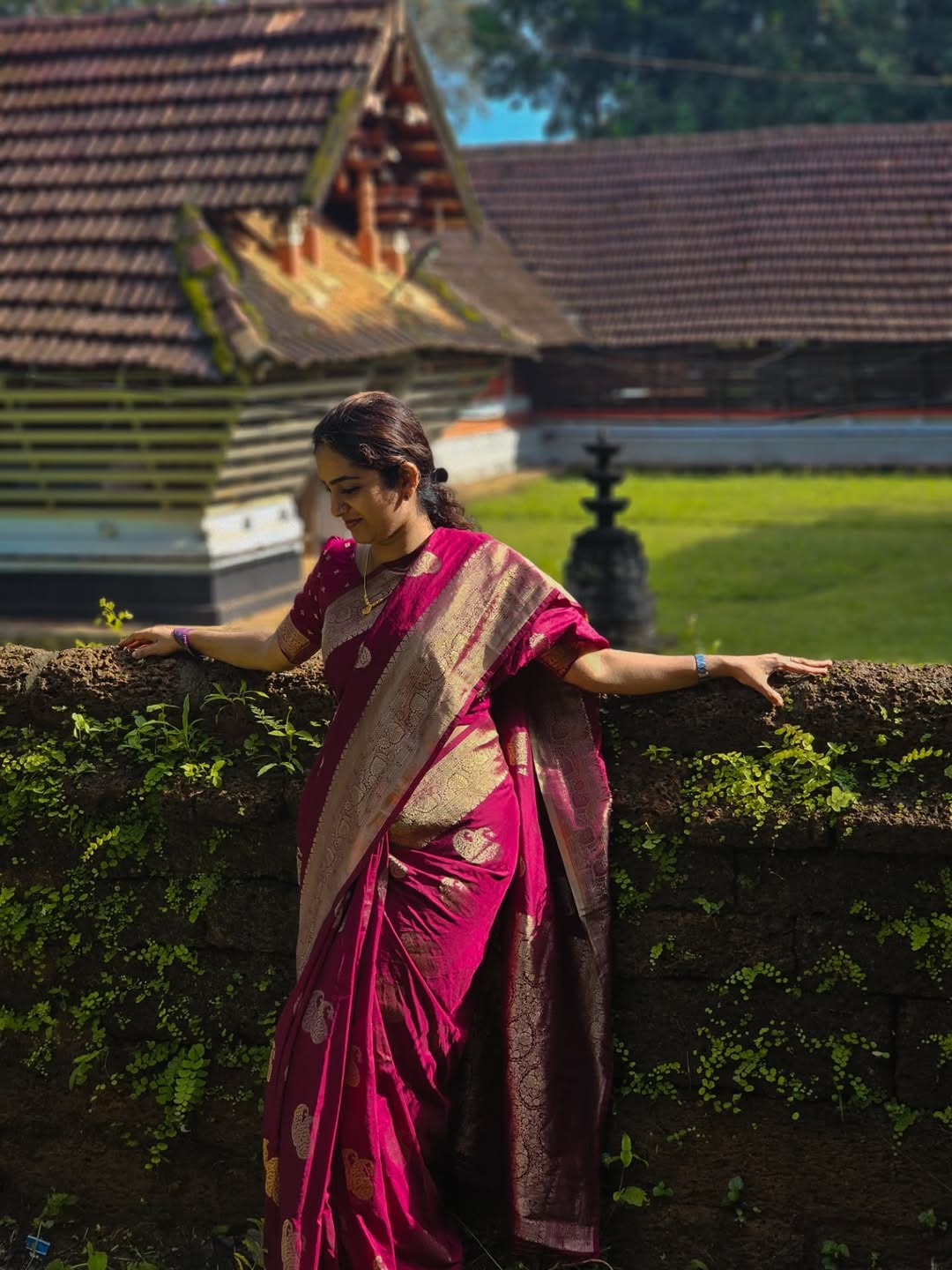 Woman in a pink saree standing in front of traditional architecture