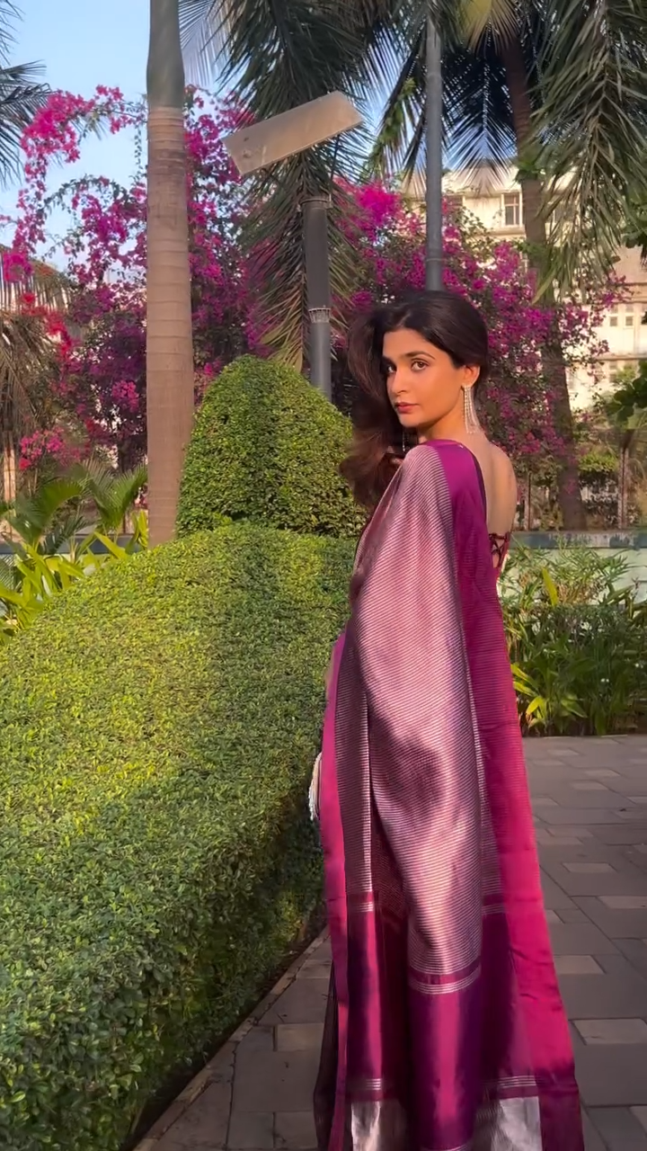 Woman in a pink saree walking in a garden with greenery and flowers.