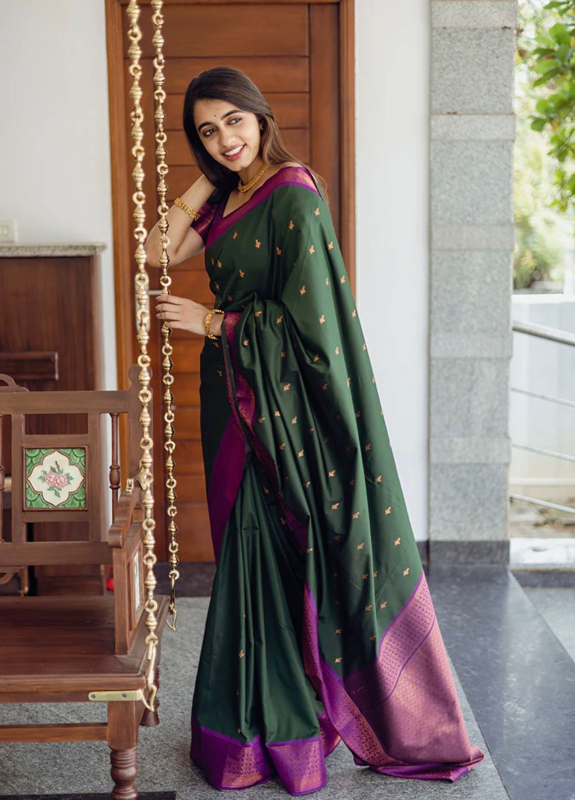 Deep forest green Banarasi Silk saree with small gold zari buttis and a striking magenta contrast border, worn by a model in an outdoor setting.