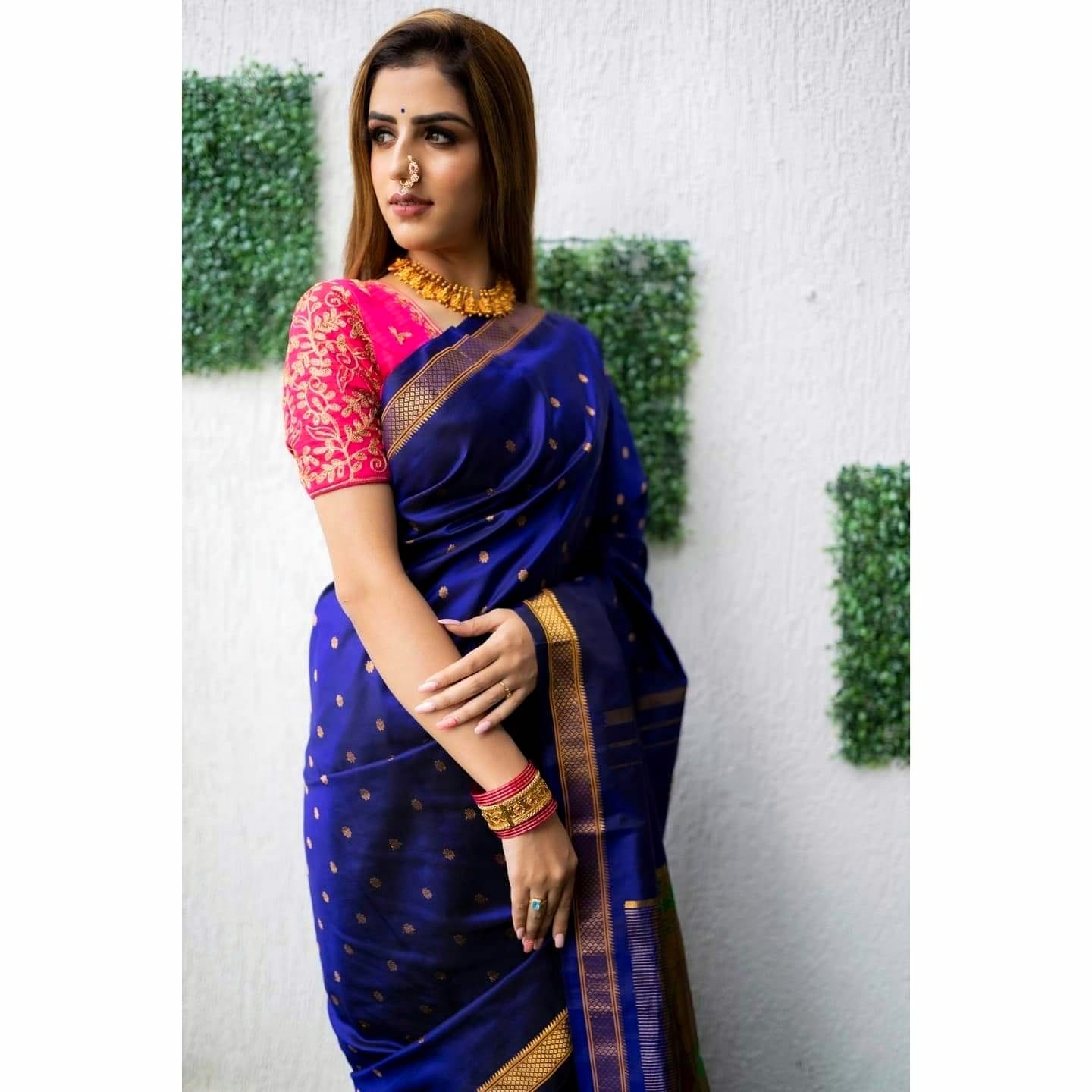 Exquisite Soft Lichi Silk saree in deep royal blue with gold circular motifs, featuring a magnificent multi-coloured Paithani-style pallu with intricate gold zari weaving, worn by a woman standing by a glass door