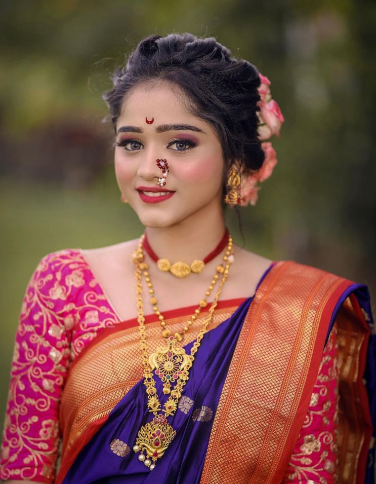 Deep amethyst purple Banarasi Soft Silk saree with scattered gold circular motifs and a bold red and gold zari woven border, beautifully styled on a woman with traditional Maharashtrian jewelry in an outdoor setting.