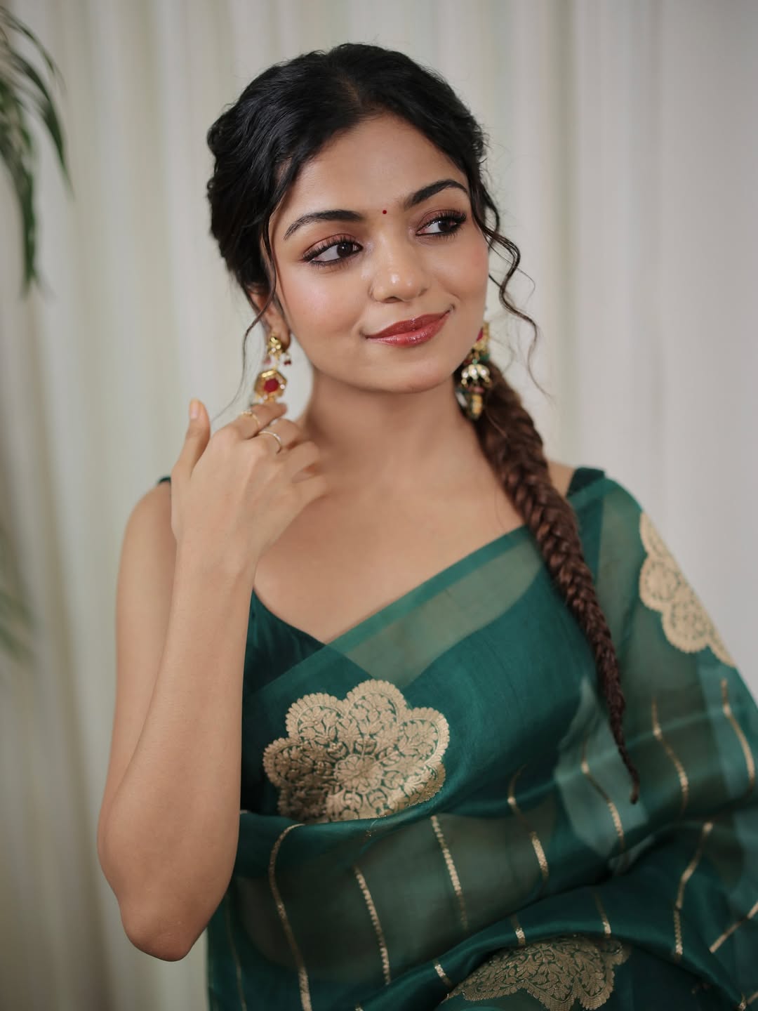 Woman wearing a green saree with gold embroidery against a white curtain background