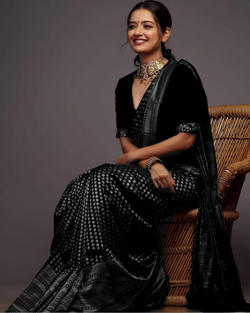 A woman models a black soft Lichi silk saree with silver patterned weaving, a matching velvet blouse, and traditional Indian jewelry, against a plain background.