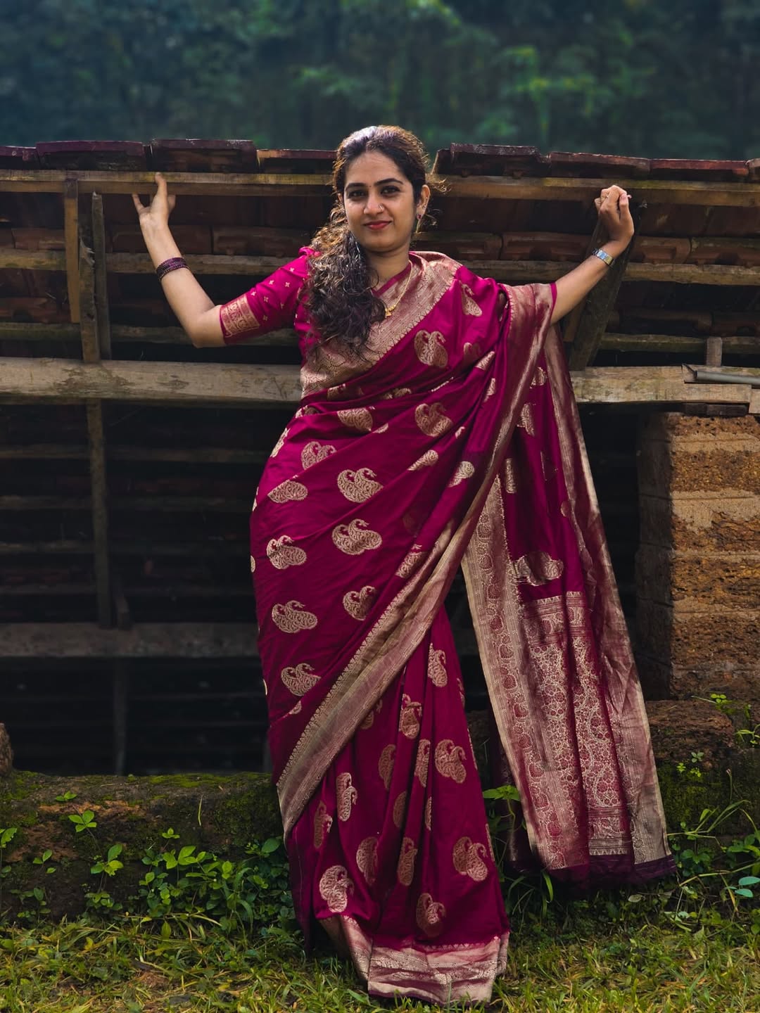 Woman in a pink saree with a pattern standing outdoors.