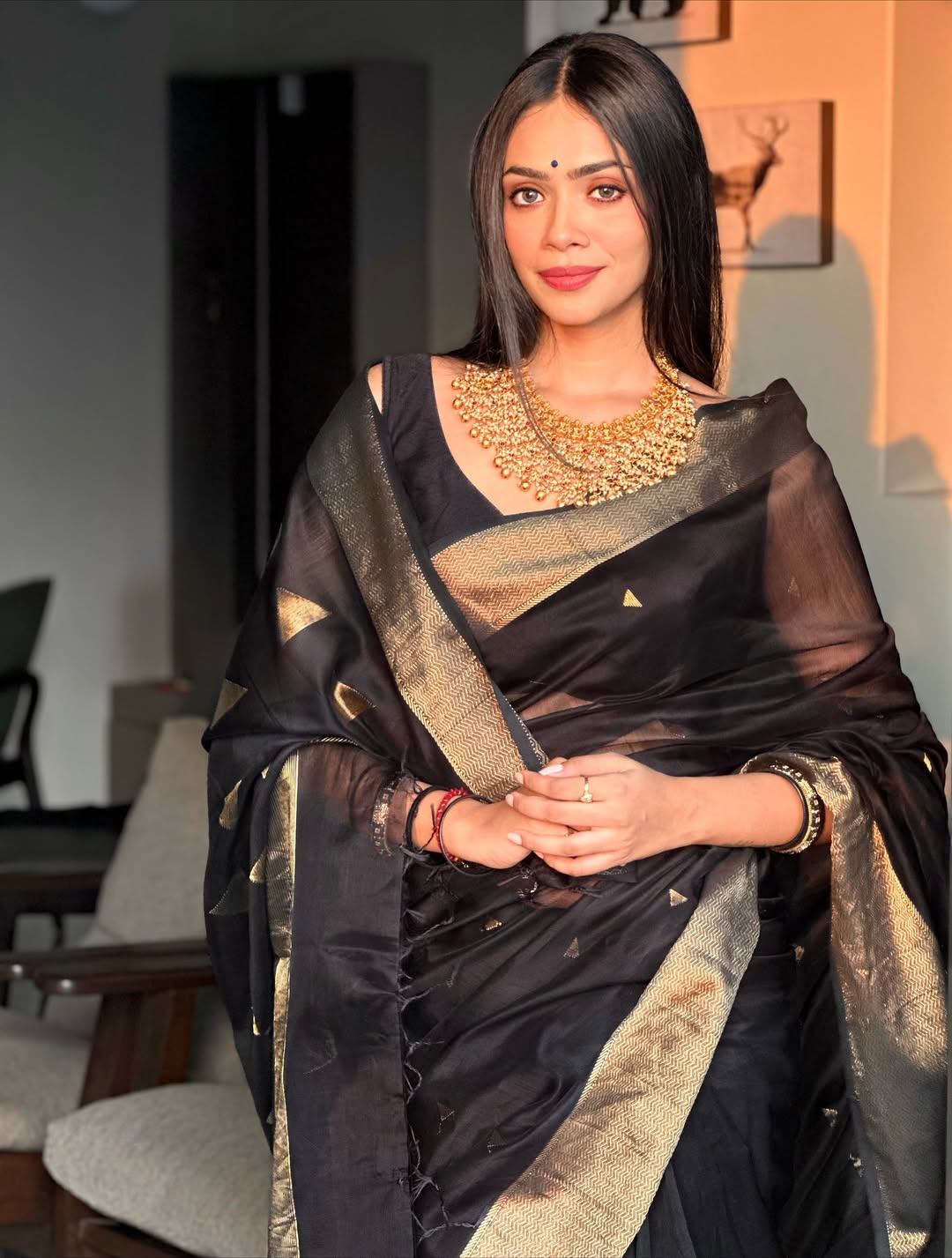 Woman in a black saree with gold patterns indoors