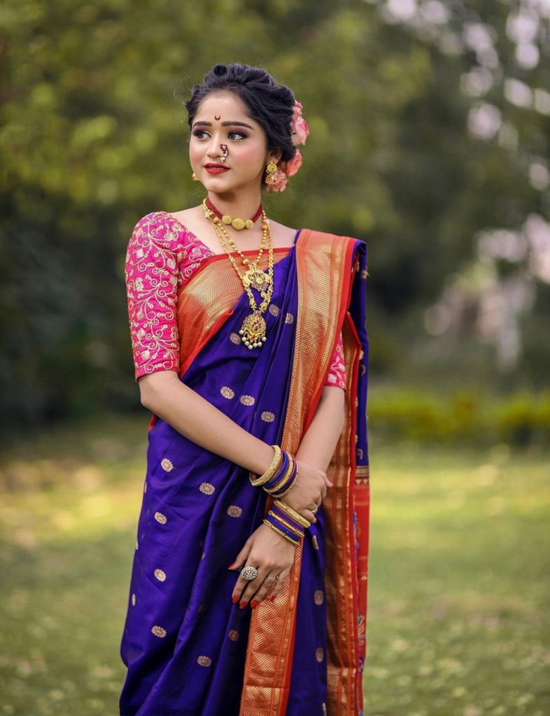 Deep amethyst purple Banarasi Soft Silk saree with scattered gold circular motifs and a bold red and gold zari woven border, beautifully styled on a woman with traditional Maharashtrian jewelry in an outdoor setting.