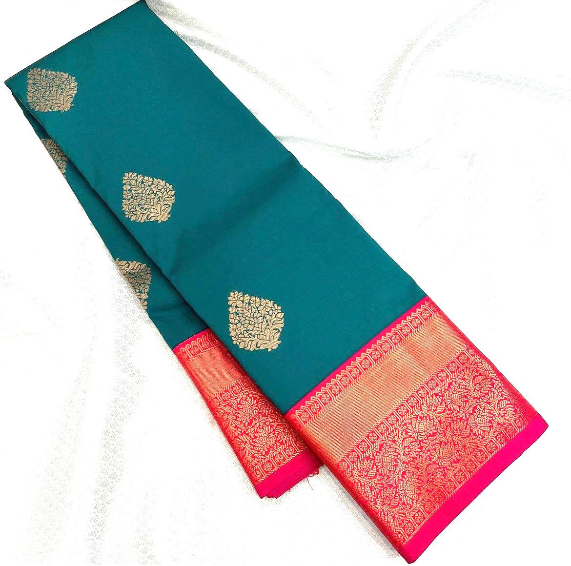 Teal/Peacock Green Banarasi Silk saree with scattered gold zari leaf motifs and a vibrant hot pink and gold zari woven contrast border and pallu, elegantly draped on a white surface.