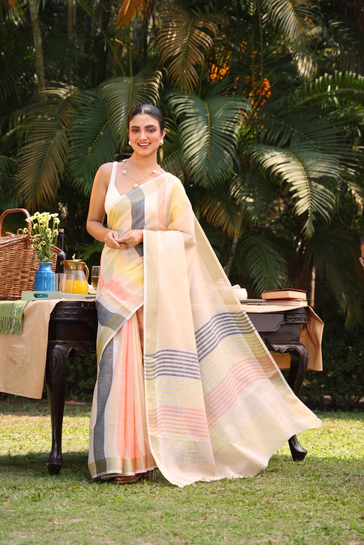 Linen silk saree, multicolor stripes, zari border, contrast blouse, weaving concept, handloom saree, Indian ethnic wear, traditional attire, women's fashion, elegant saree, summer saree, outdoor photoshoot, garden setting, model wearing saree, designer saree, striped saree, lightweight saree, breathable fabric, ethnic fashion, traditional Indian saree.