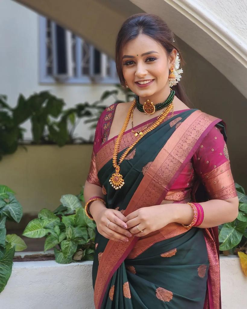 Royal purple Banarasi Silk saree with large rose gold zari paisley motifs and a heavy woven border, worn by a woman holding a small pink potli bag.