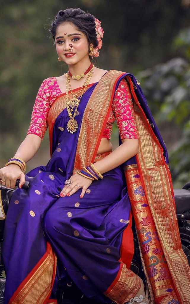 Deep amethyst purple Banarasi Soft Silk saree with scattered gold circular motifs and a bold red and gold zari woven border, beautifully styled on a woman with traditional Maharashtrian jewelry in an outdoor setting.