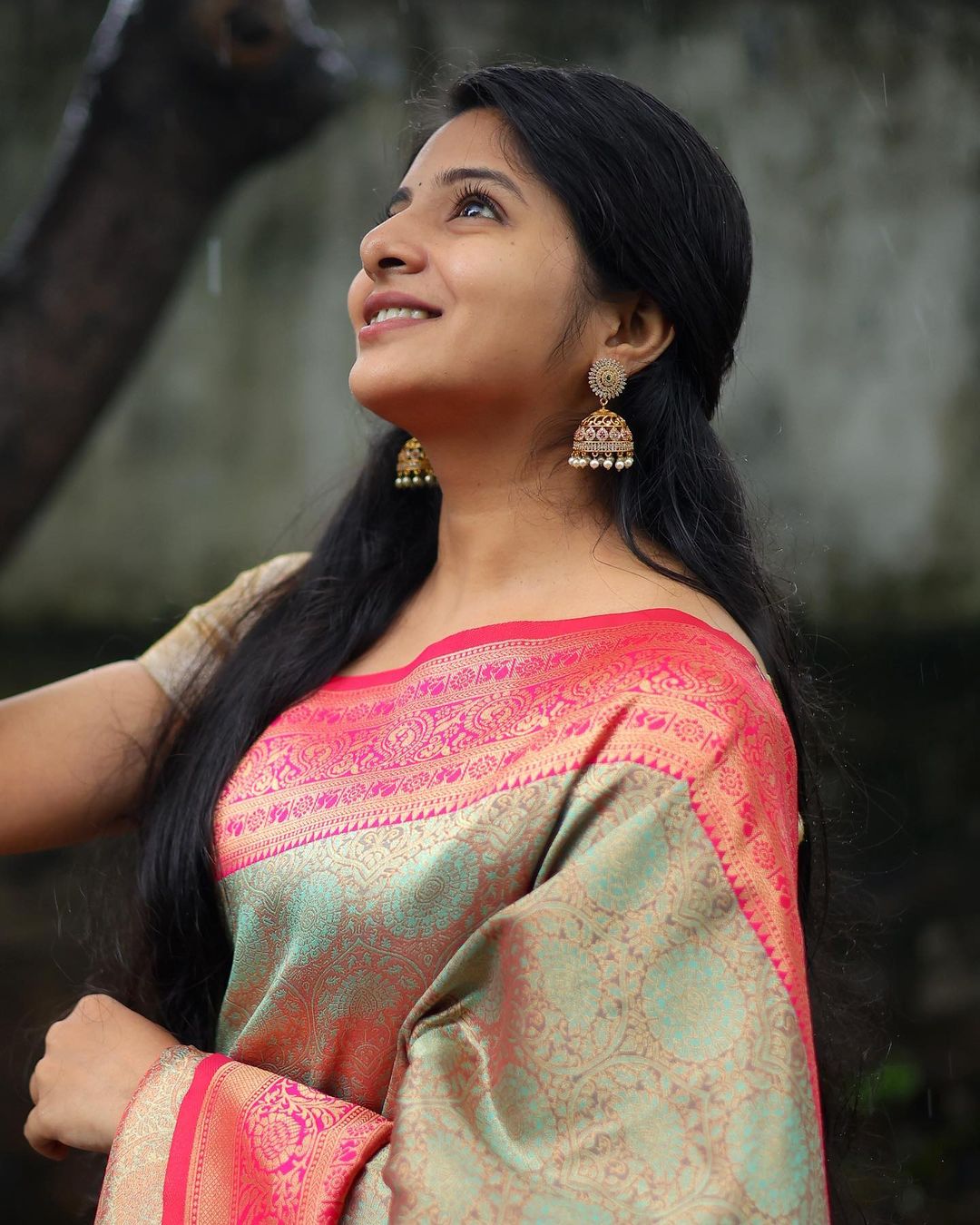 Green Banarasi soft silk saree with red gold zari border worn by model on outdoor rainy pathway