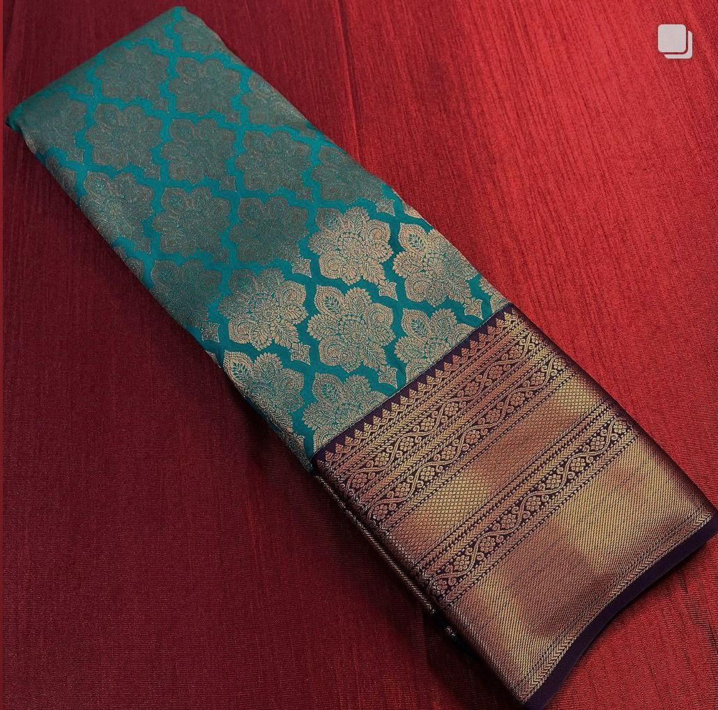 Teal Banarasi Silk saree with an all-over copper/bronze zari floral jaal body and a wide antique-finish copper zari border, beautifully draped on a white surface.