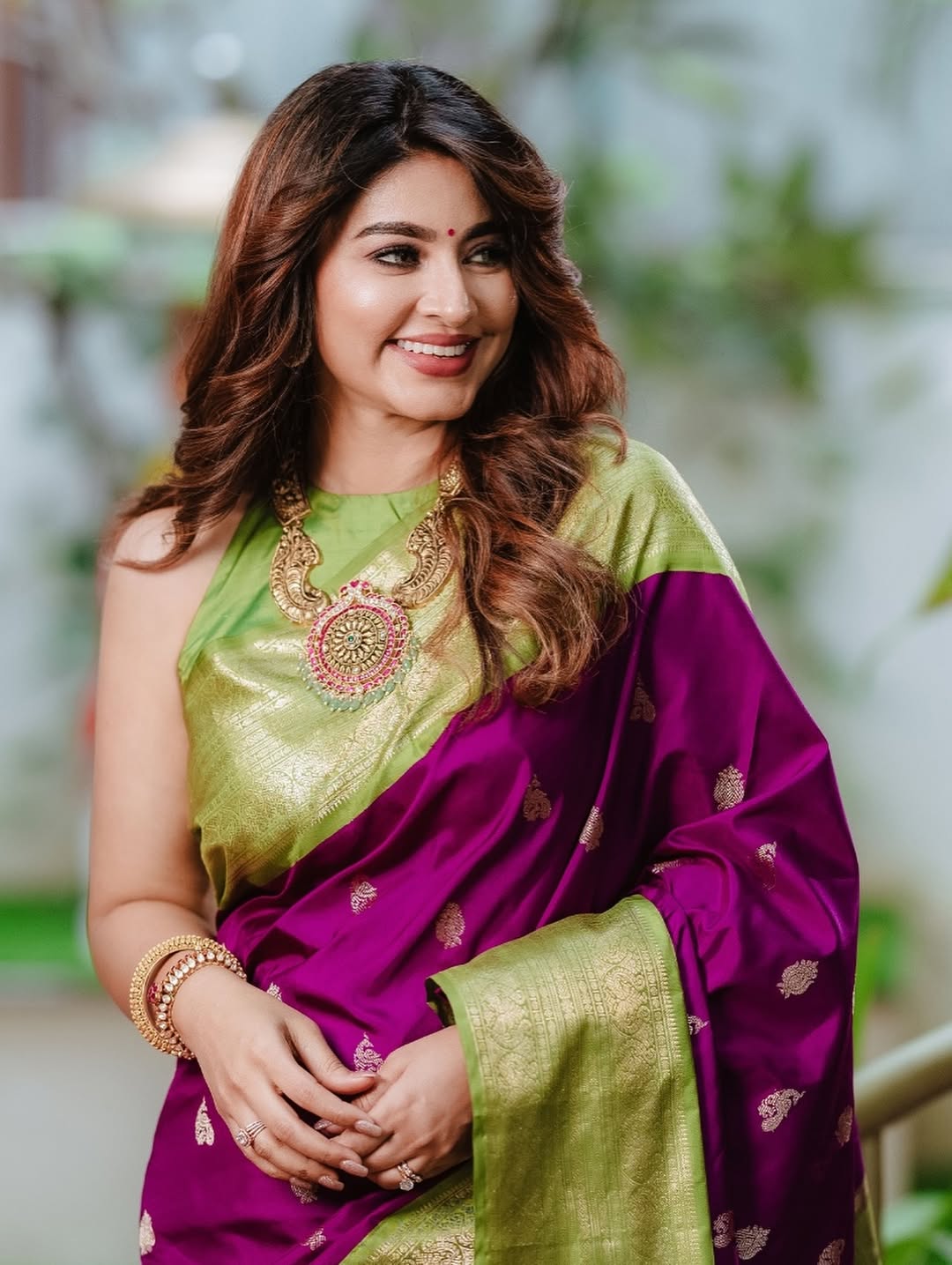 Woman wearing a purple and green saree with a blurred natural background