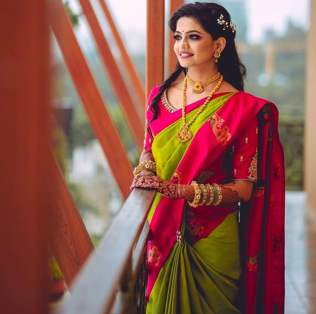 Radiant Soft Lichi Silk saree in lime green with subtle self-weaves, featuring a vibrant fuchsia pink pallu and border with intricate gold zari motifs, worn by a smiling woman on a balcony