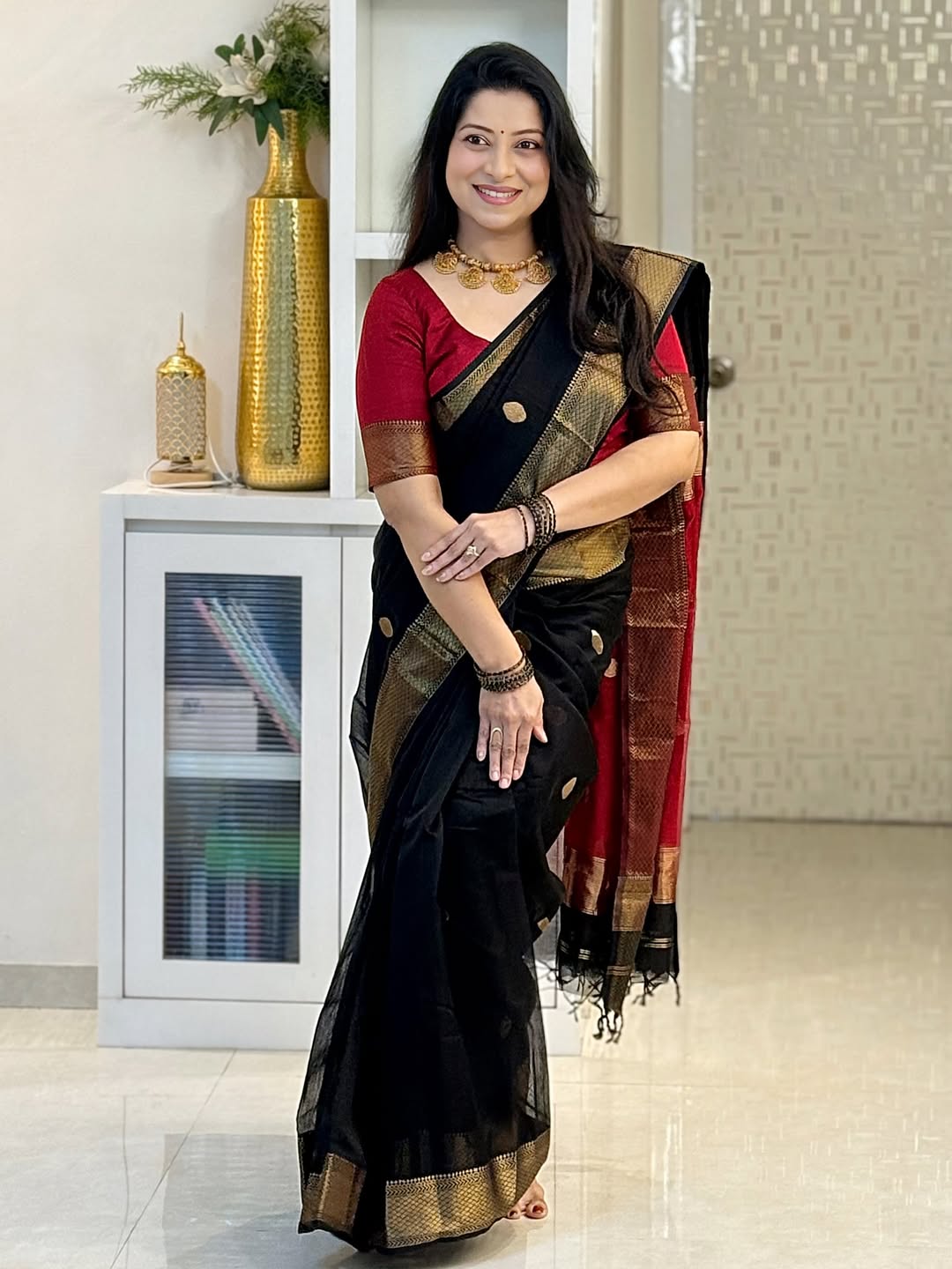 Woman in a black saree with gold patterns standing indoors.