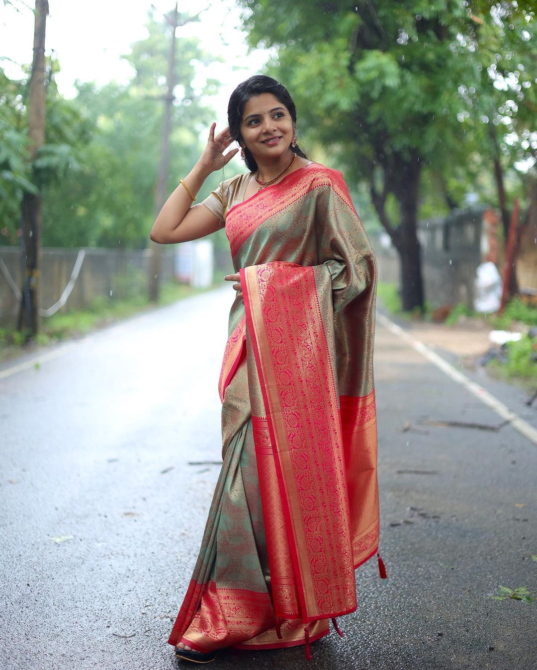 Green Banarasi soft silk saree with red gold zari border worn by model on outdoor rainy pathway