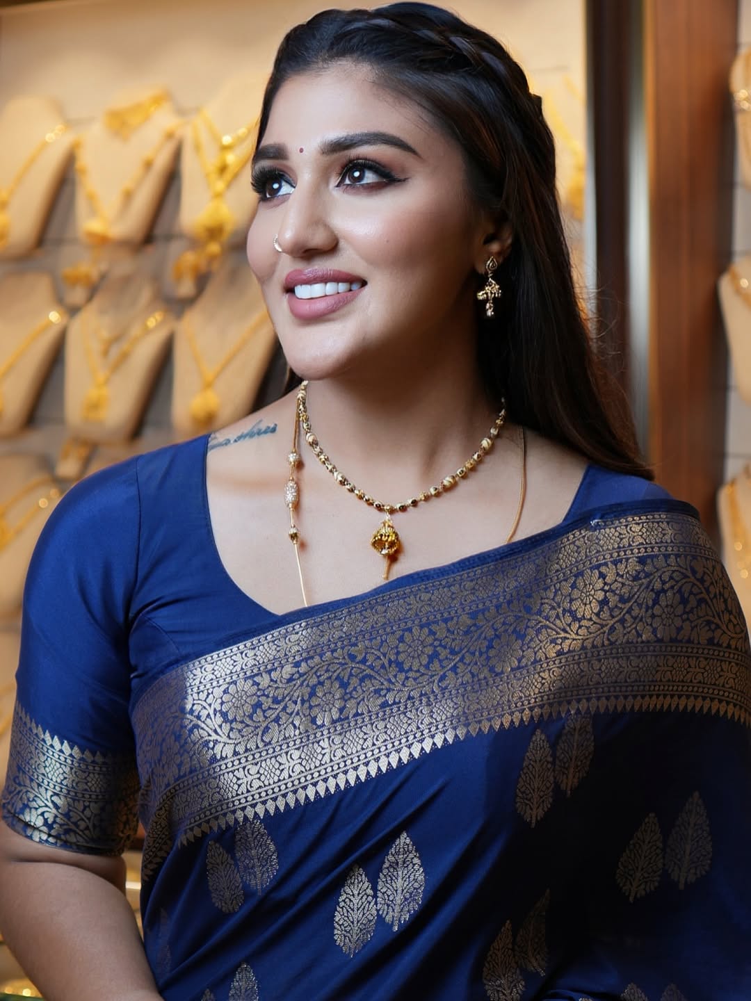Woman wearing a blue saree with gold details in front of a jewelry display.