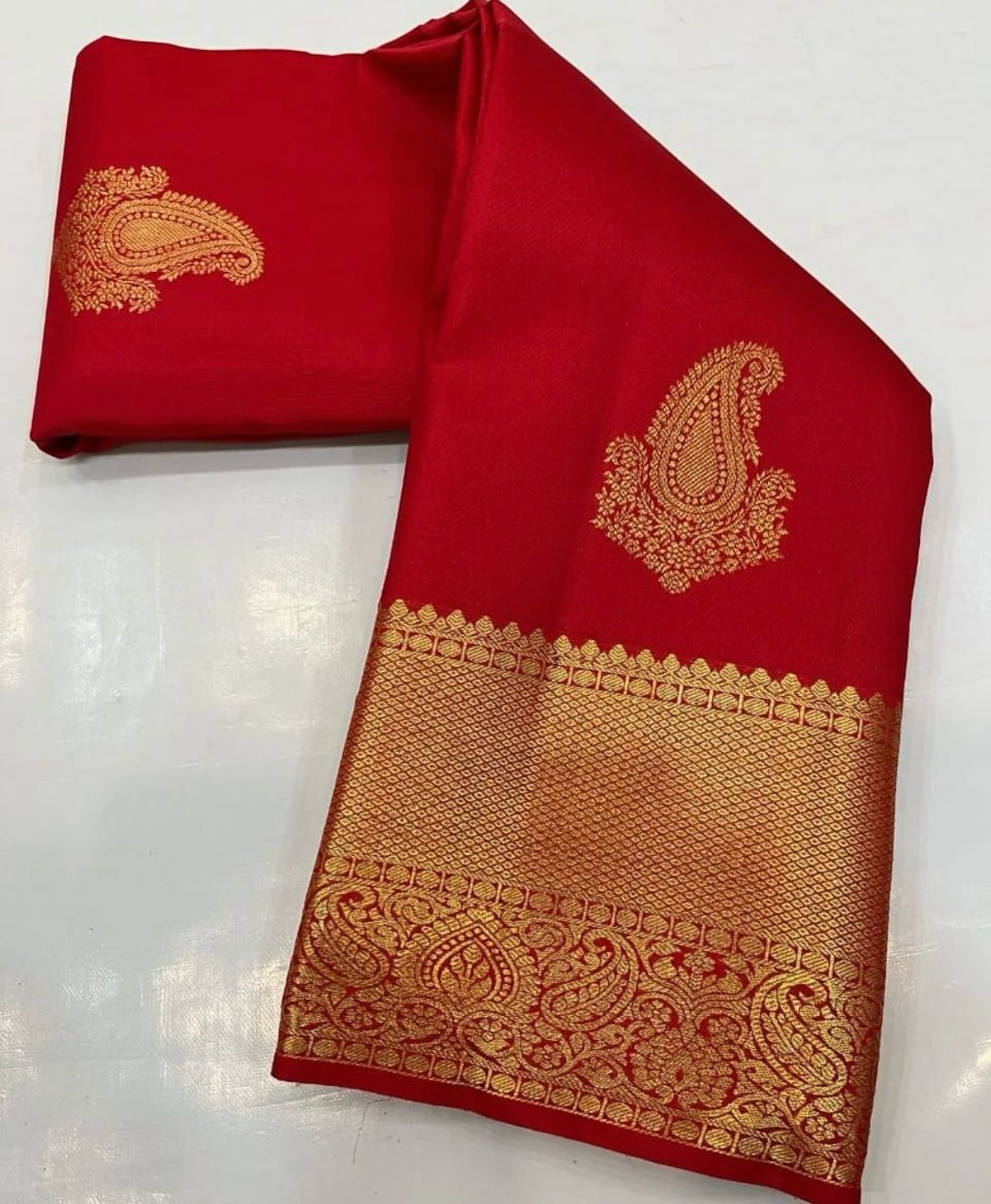 Vibrant rich red Banarasi Silk saree with scattered gold zari mango (paisley) buttas and a wide, intricately woven gold zari border and pallu, elegantly draped on a white surface.