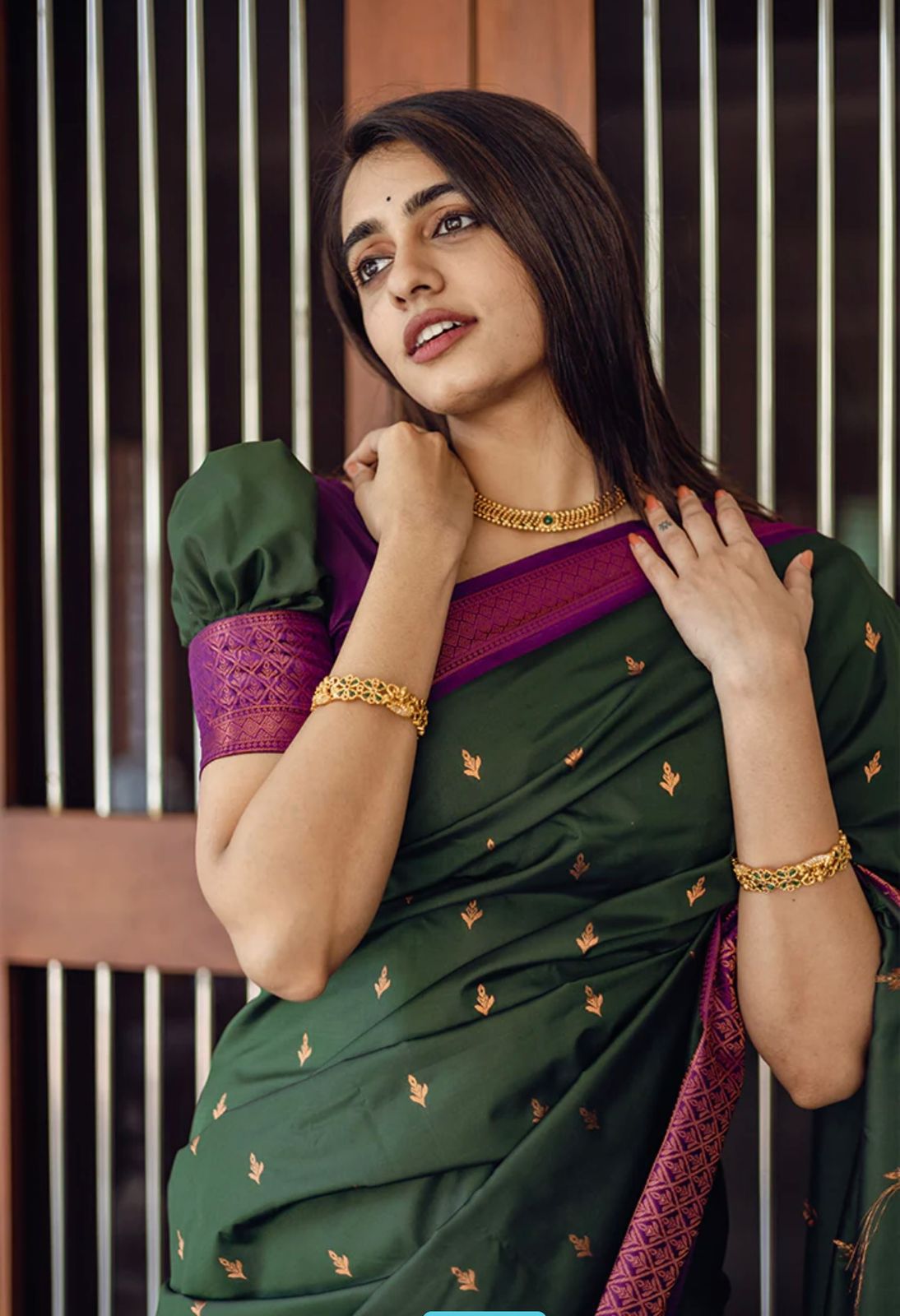 Deep forest green Banarasi Silk saree with small gold zari buttis and a striking magenta contrast border, worn by a model in an outdoor setting.