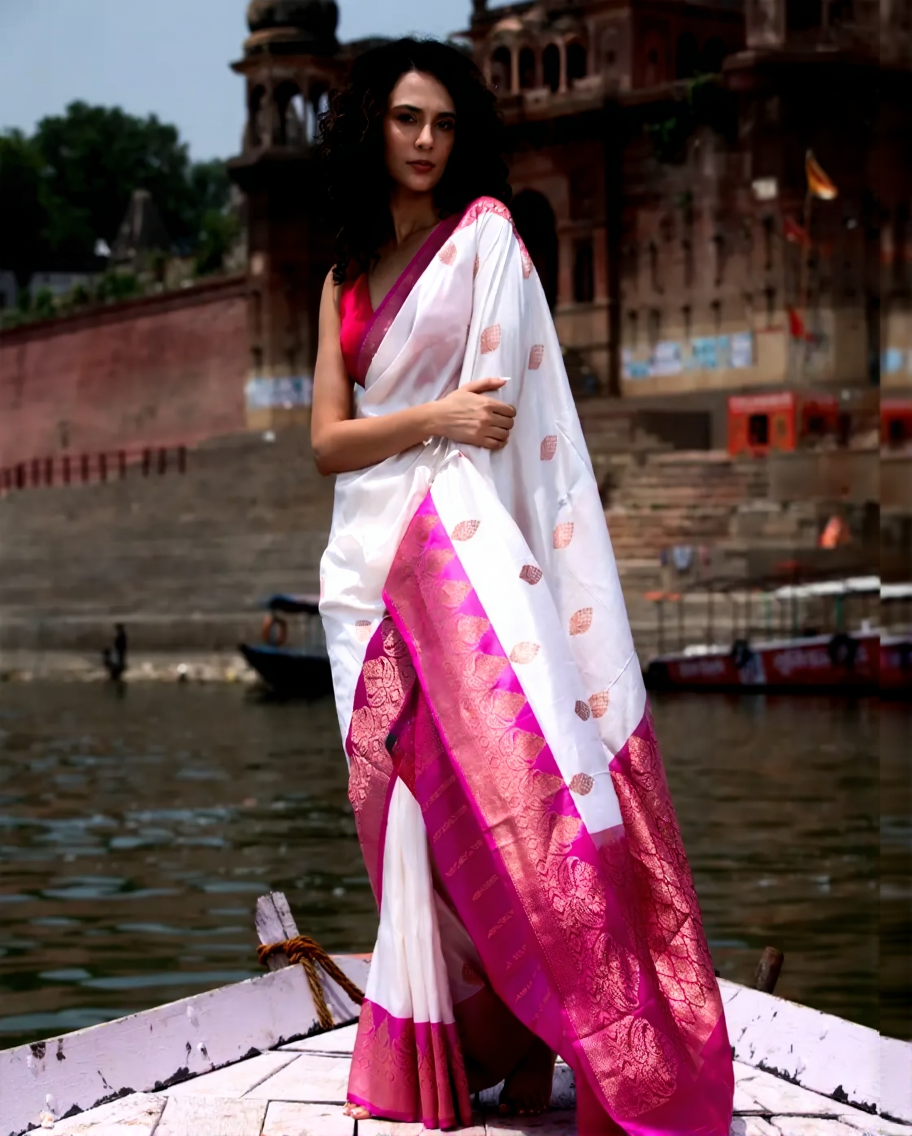 Woman in a white and pink saree standing on a boat with a historical building in the background.