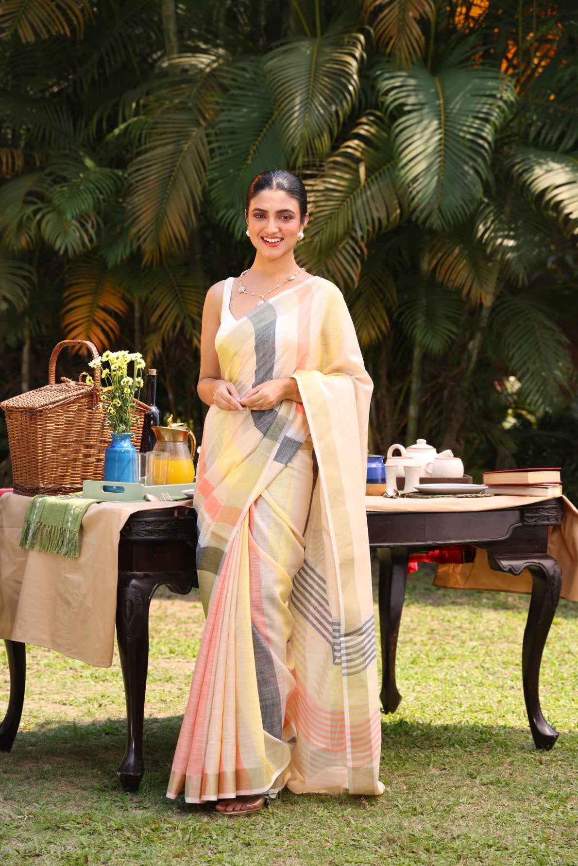 Linen silk saree, multicolor stripes, zari border, contrast blouse, weaving concept, handloom saree, Indian ethnic wear, traditional attire, women's fashion, elegant saree, summer saree, outdoor photoshoot, garden setting, model wearing saree, designer saree, striped saree, lightweight saree, breathable fabric, ethnic fashion, traditional Indian saree.