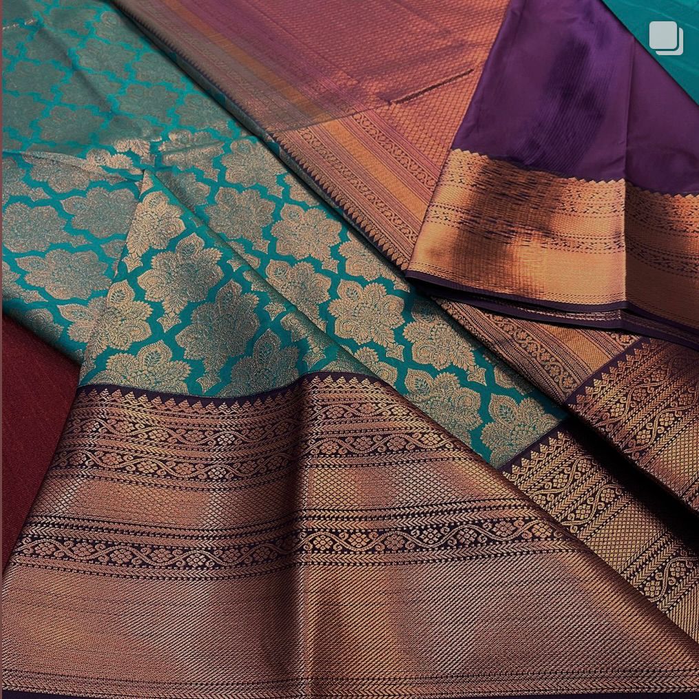 Teal Banarasi Silk saree with an all-over copper/bronze zari floral jaal body and a wide antique-finish copper zari border, beautifully draped on a white surface.