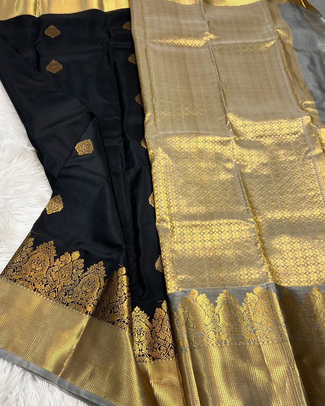Classic jet black Banarasi Silk saree with scattered gold zari motifs, a wide intricately woven gold zari border, and a shimmering gold/silver zari contrast pallu, elegantly draped on a white textured surface.