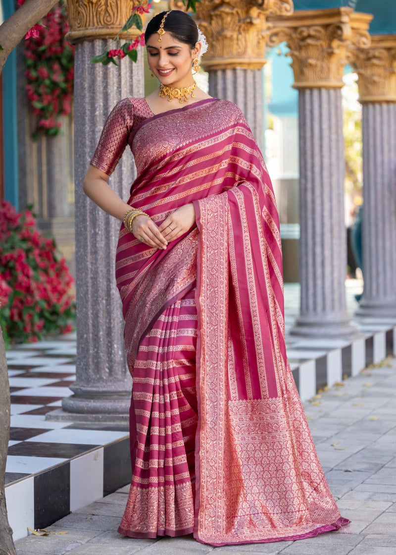 Woman in a pink saree standing in front of classical architecture with flowers around.