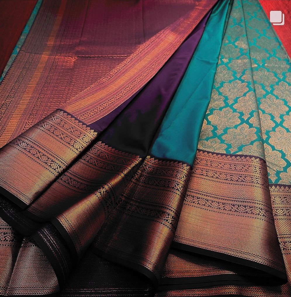Teal Banarasi Silk saree with an all-over copper/bronze zari floral jaal body and a wide antique-finish copper zari border, beautifully draped on a white surface.