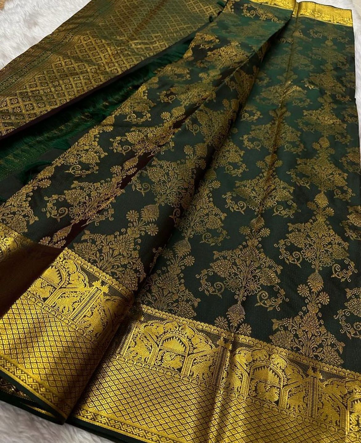 Deep forest green Banarasi Silk saree with dense all-over gold zari floral weaving and a wide border featuring traditional elephant motifs and geometric patterns, elegantly draped on a white textured surface.
