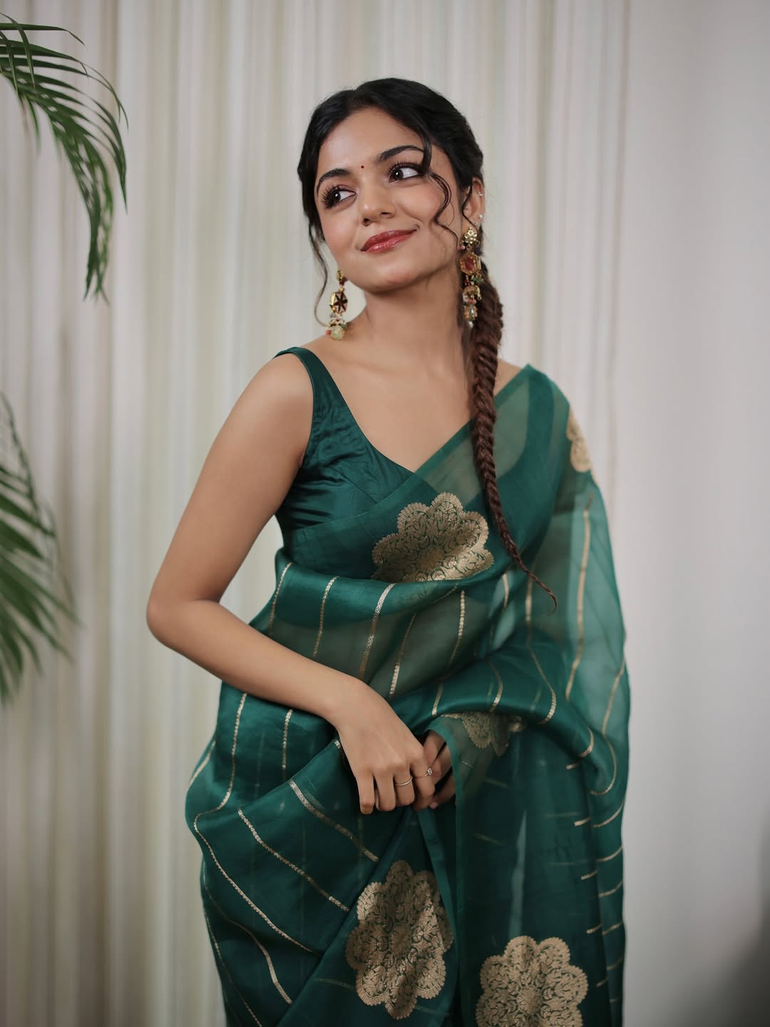 Woman in a green saree with gold patterns against a white curtain background