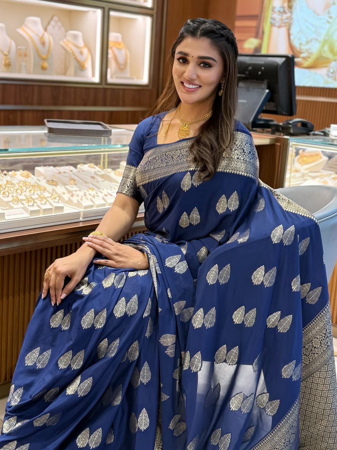 Woman in a blue saree with silver patterns sitting in a jewelry store.
