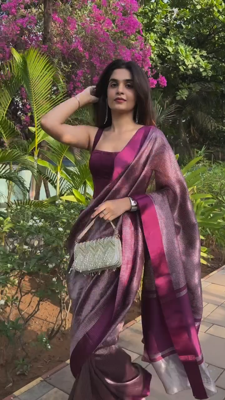 Woman in a purple saree standing outdoors with greenery in the background