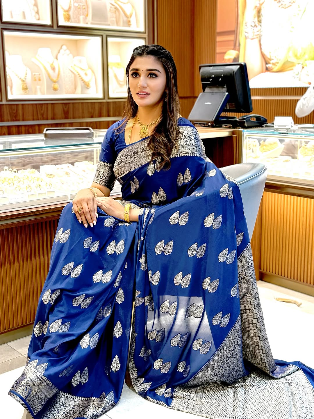 Woman in a blue saree with silver patterns sitting in a jewelry store.