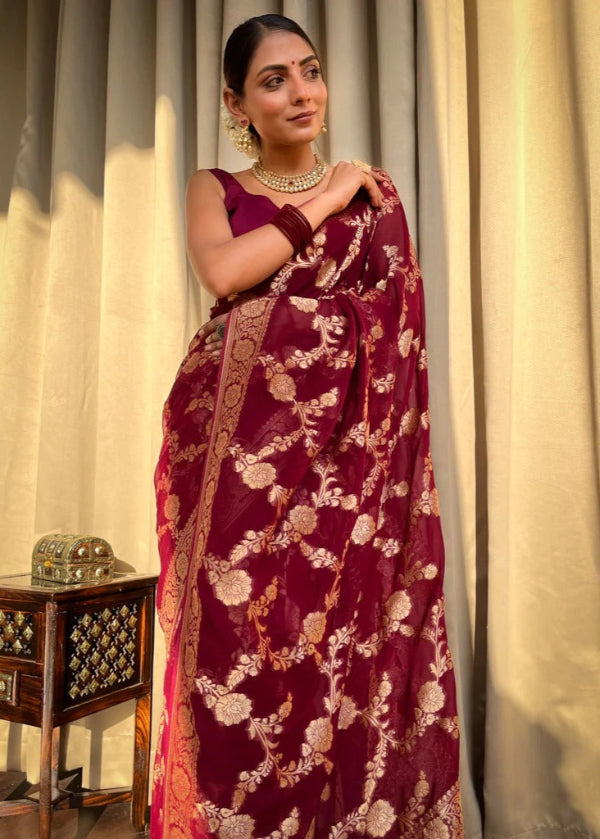 Woman wearing a maroon saree with gold patterns against a neutral curtain background