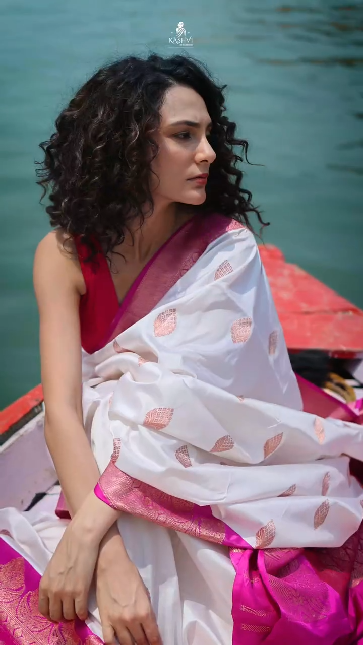 Woman in a white saree with pink blouse sitting on a boat with water in the background