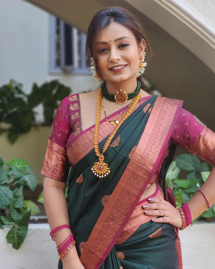 Royal purple Banarasi Silk saree with large rose gold zari paisley motifs and a heavy woven border, worn by a woman holding a small pink potli bag.