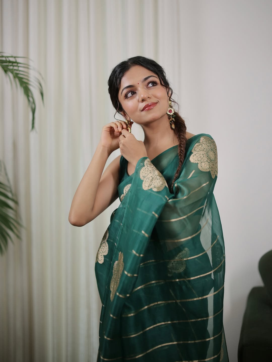 Woman wearing a green saree with gold patterns against a white curtain background