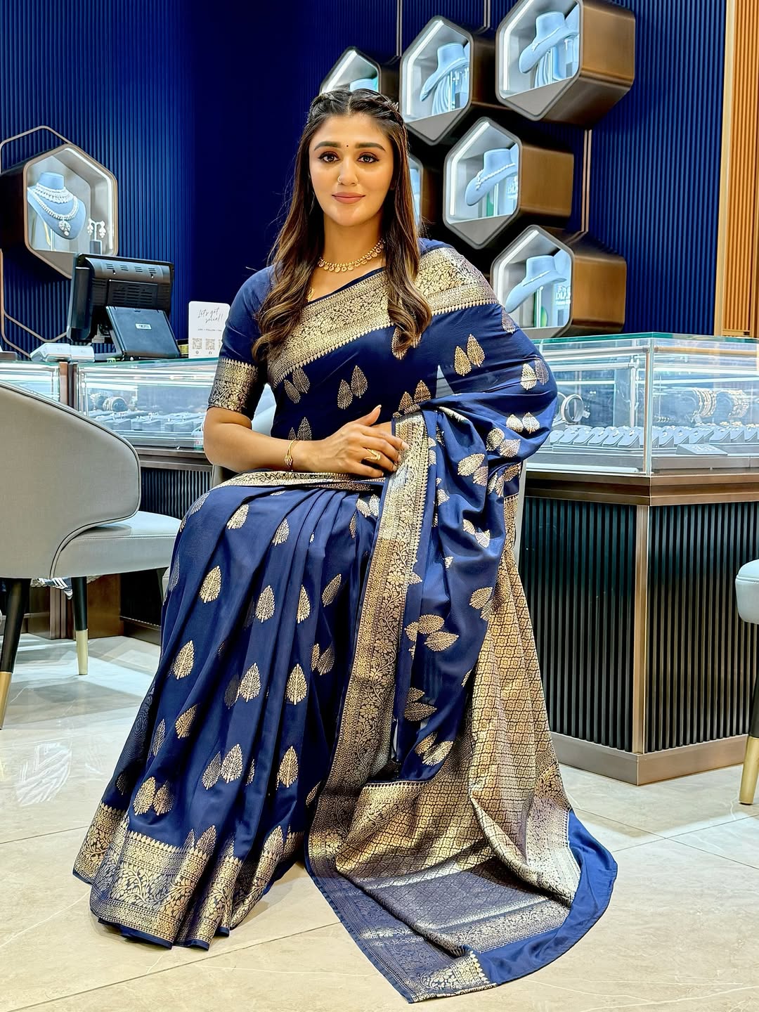 Woman in a blue saree with gold patterns indoors.