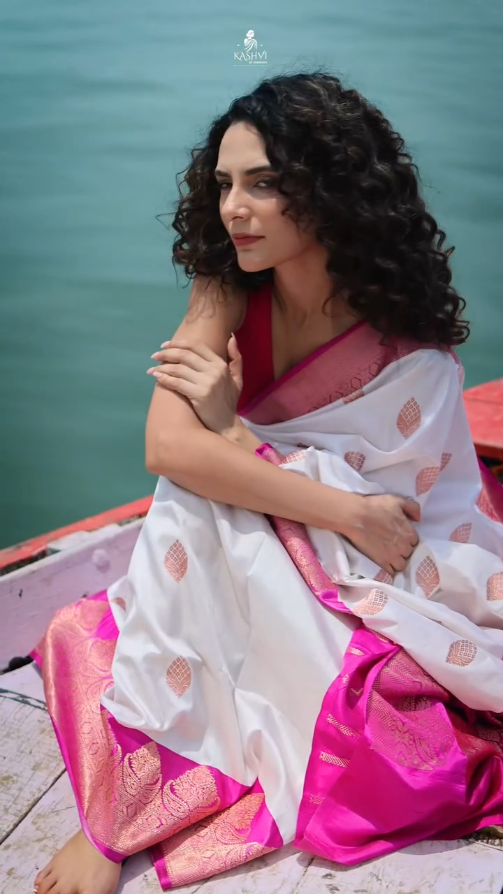 Woman in a white and pink saree sitting on a boat with water in the background