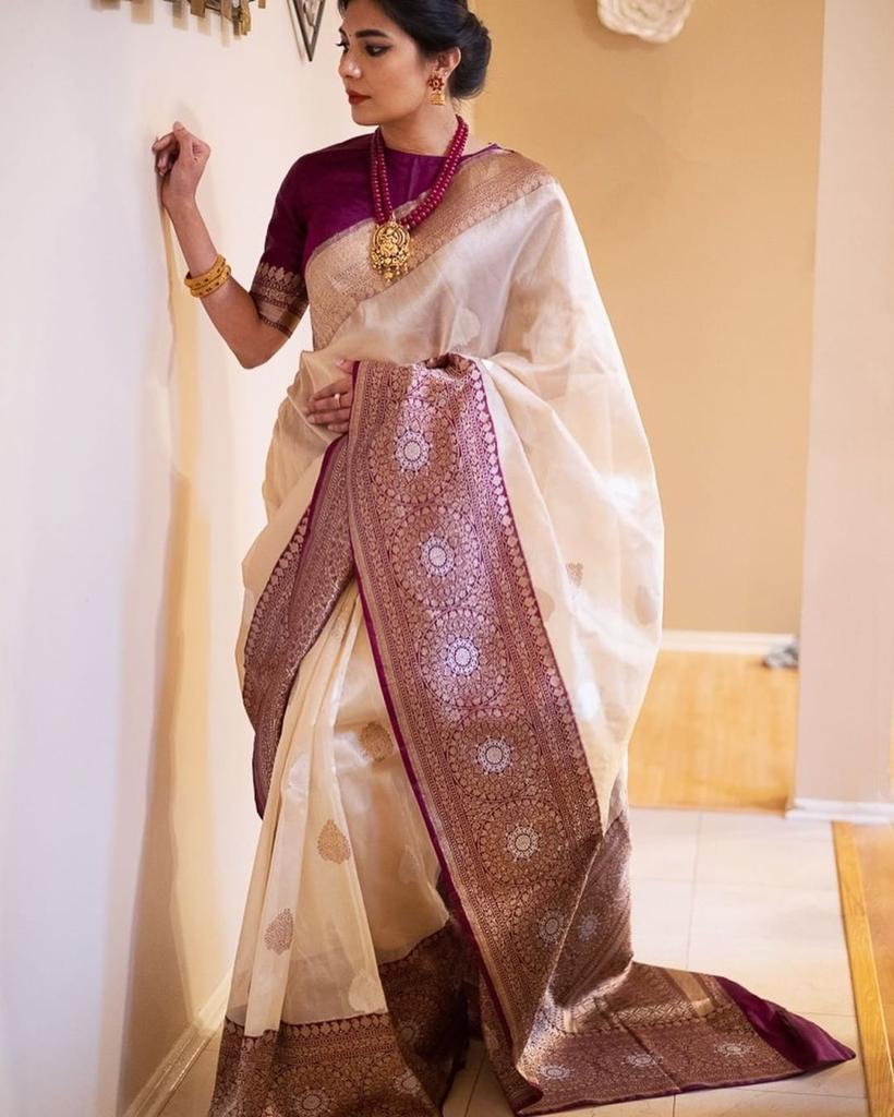 Woman wearing a traditional saree with a white and brown design, standing indoors.
