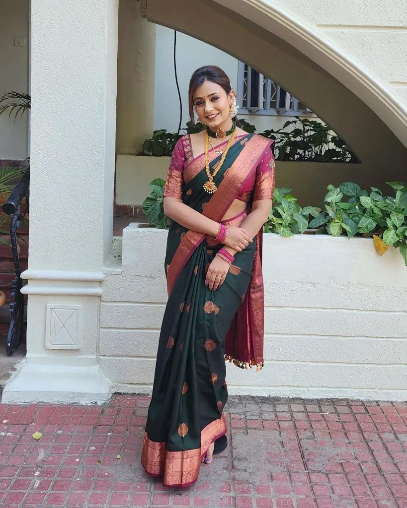 Royal purple Banarasi Silk saree with large rose gold zari paisley motifs and a heavy woven border, worn by a woman holding a small pink potli bag.