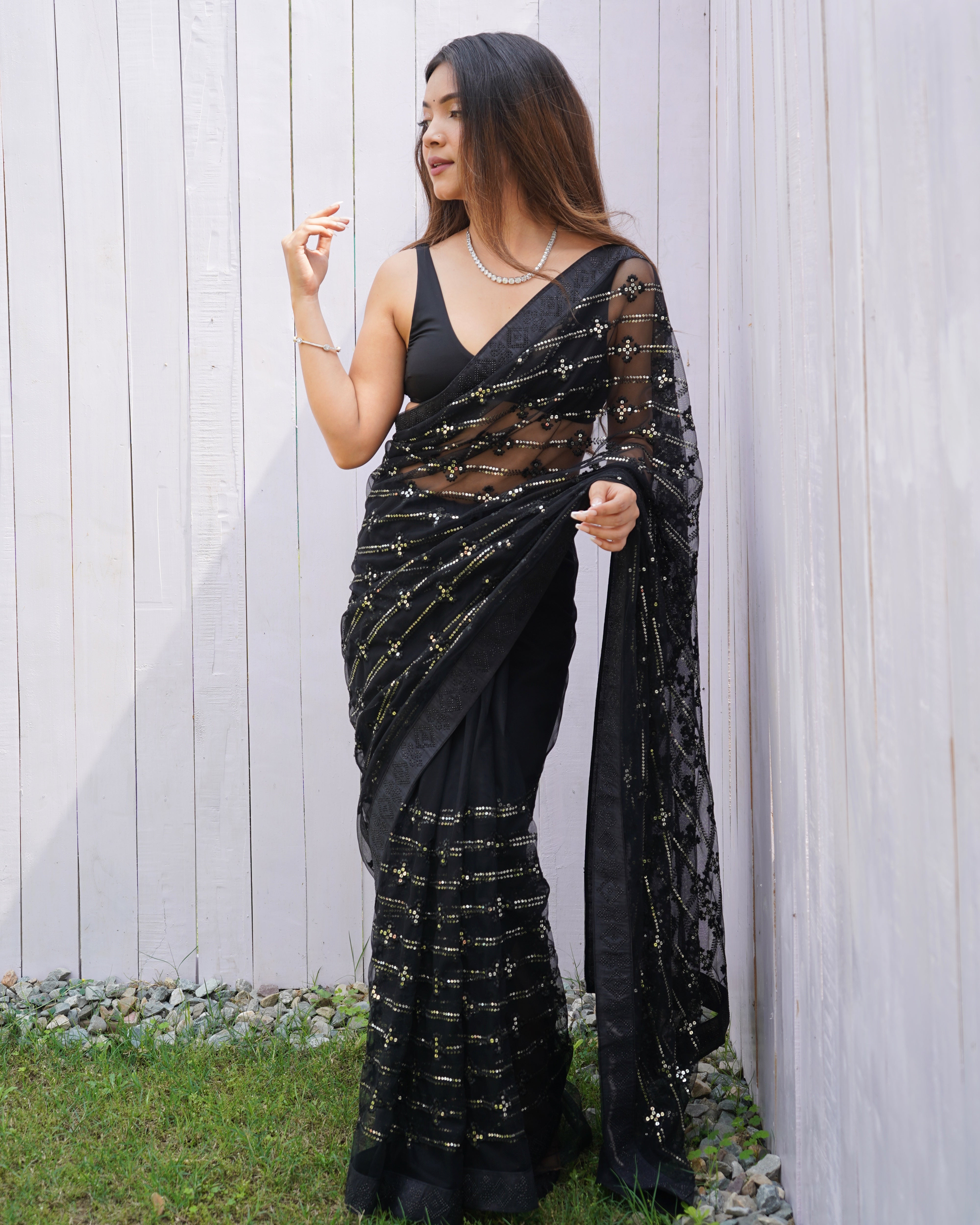 Model wearing a sheer black butterfly net saree with horizontal sequin lines and multi-thread embroidery details.
