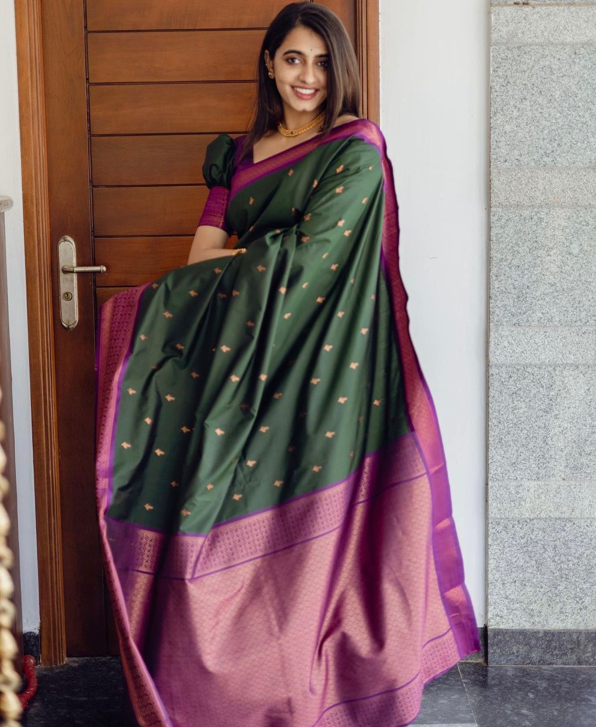Deep forest green Banarasi Silk saree with small gold zari buttis and a striking magenta contrast border, worn by a model in an outdoor setting.