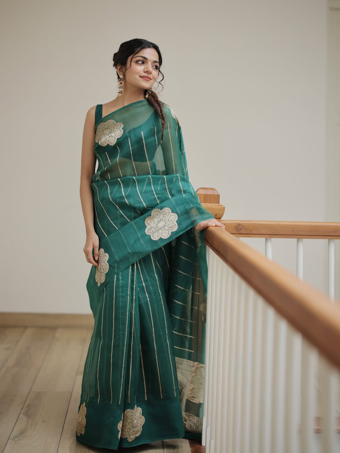 Woman wearing a green saree with floral patterns, standing indoors.