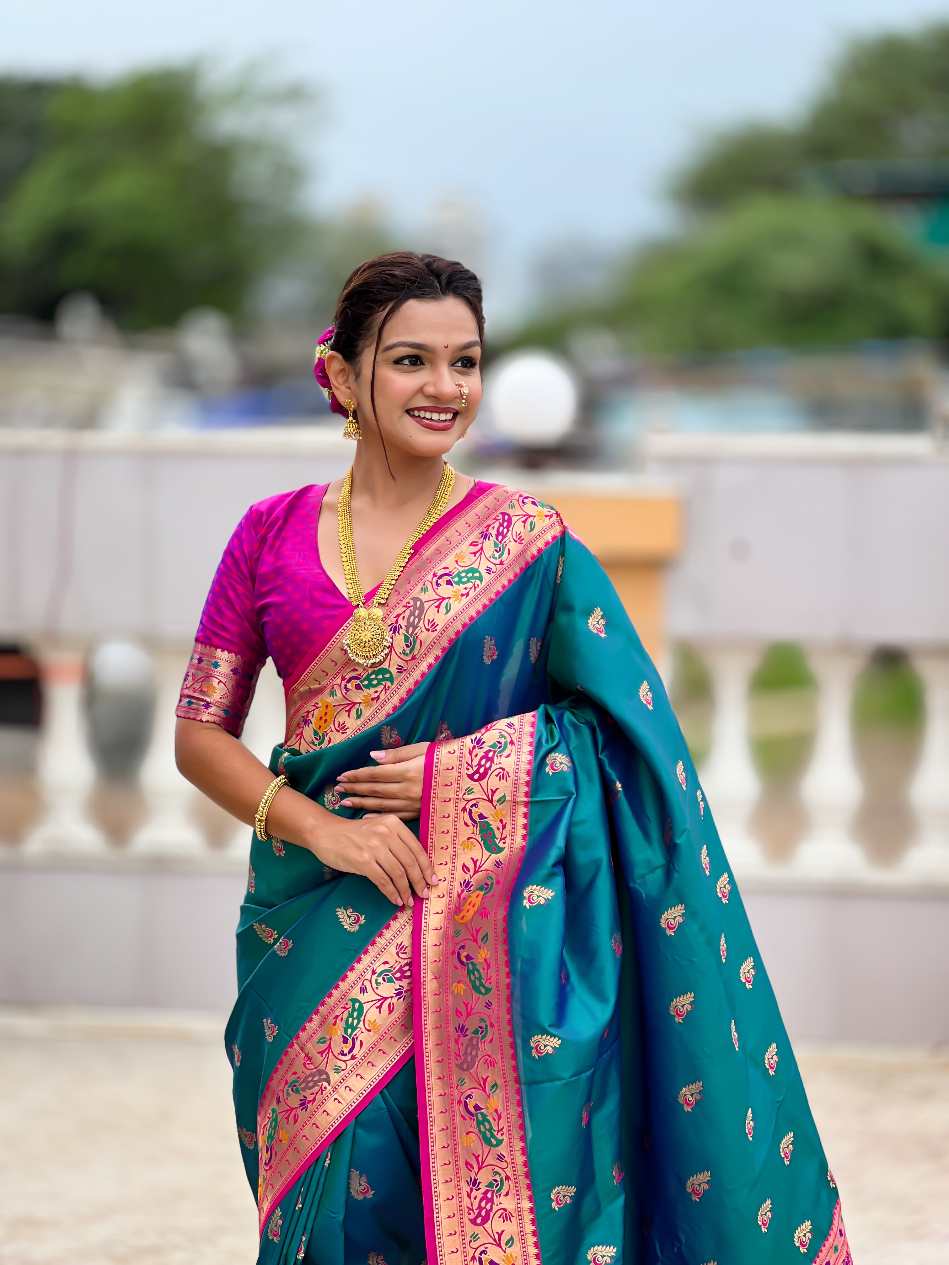 Model wearing a royal soft Paithani silk saree with Meenakari zari weaving and contrast pink border in a traditional temple setting