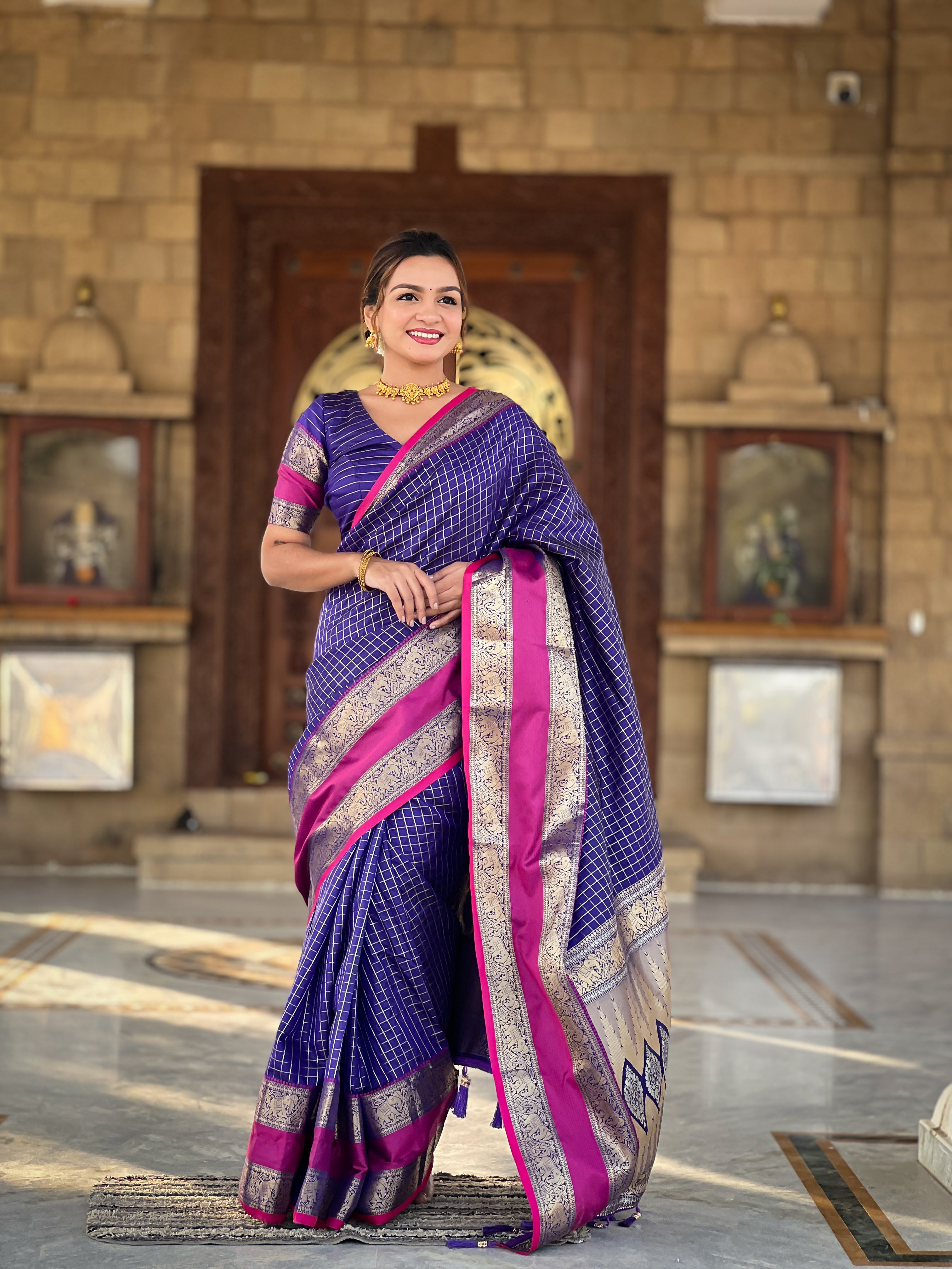 Woman wearing regal violet soft silk saree with gold zari checks, magenta contrast border, and rich pallu with tassels