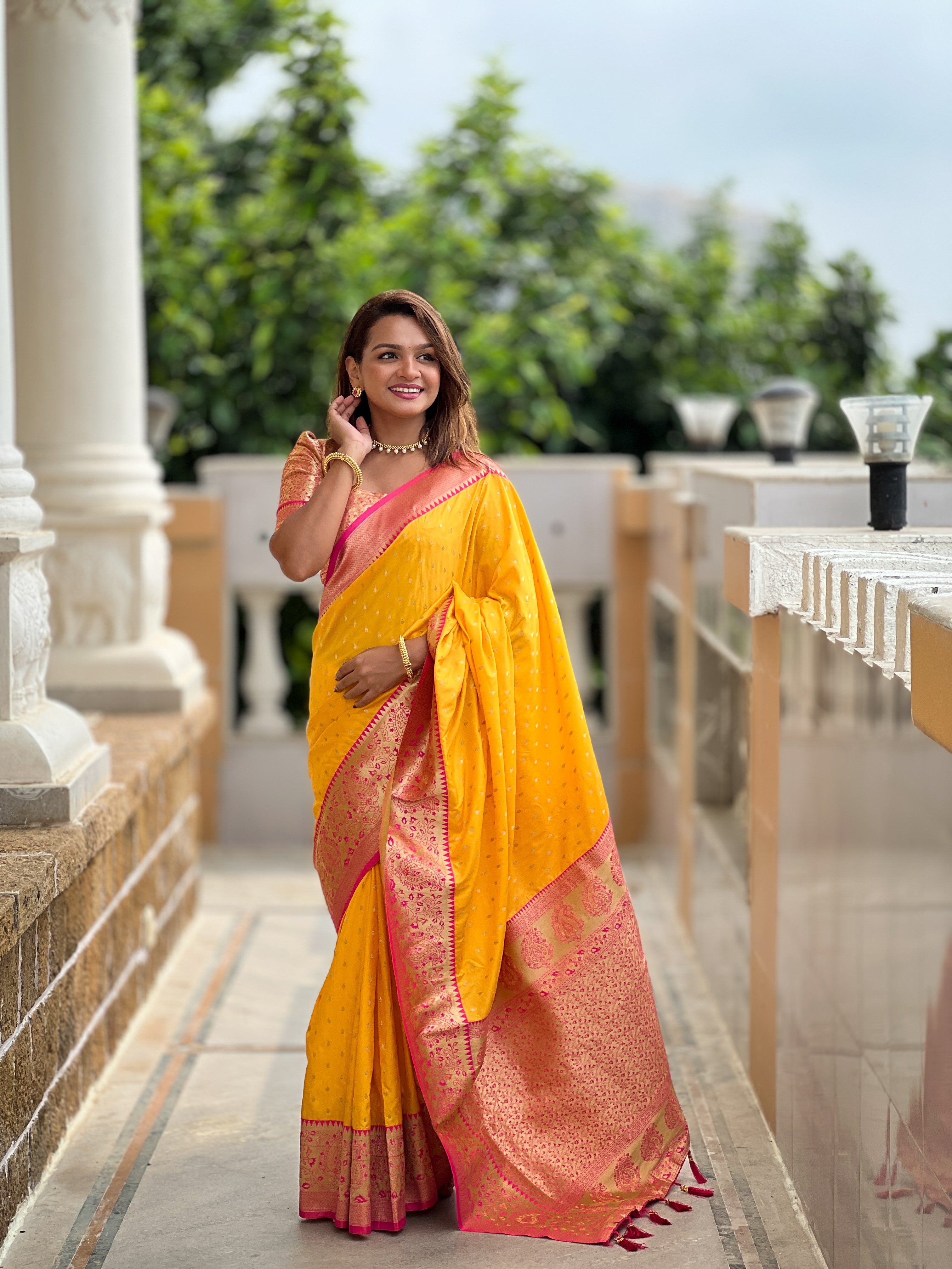 Woman wearing yellow soft silk saree with pink contrast border, gold zari motifs, and rich pallu design