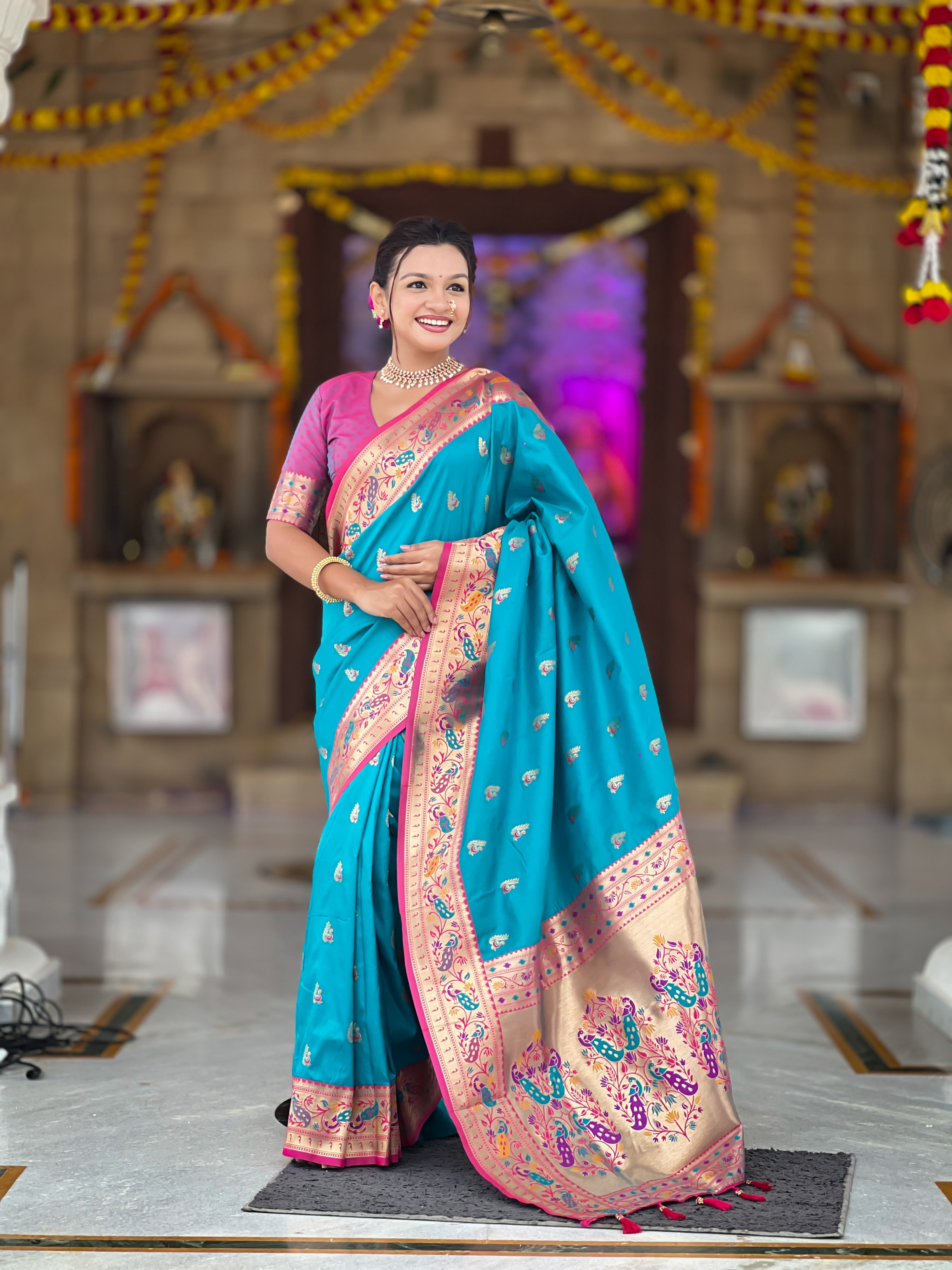 Model wearing a royal soft Paithani silk saree with Meenakari zari weaving and contrast pink border in a traditional temple setting